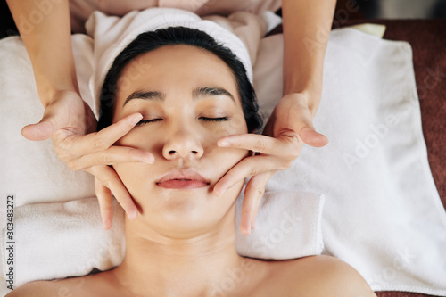 Young Asian woman lying on massage table and enjoying face massage in beauty clinic  view from above