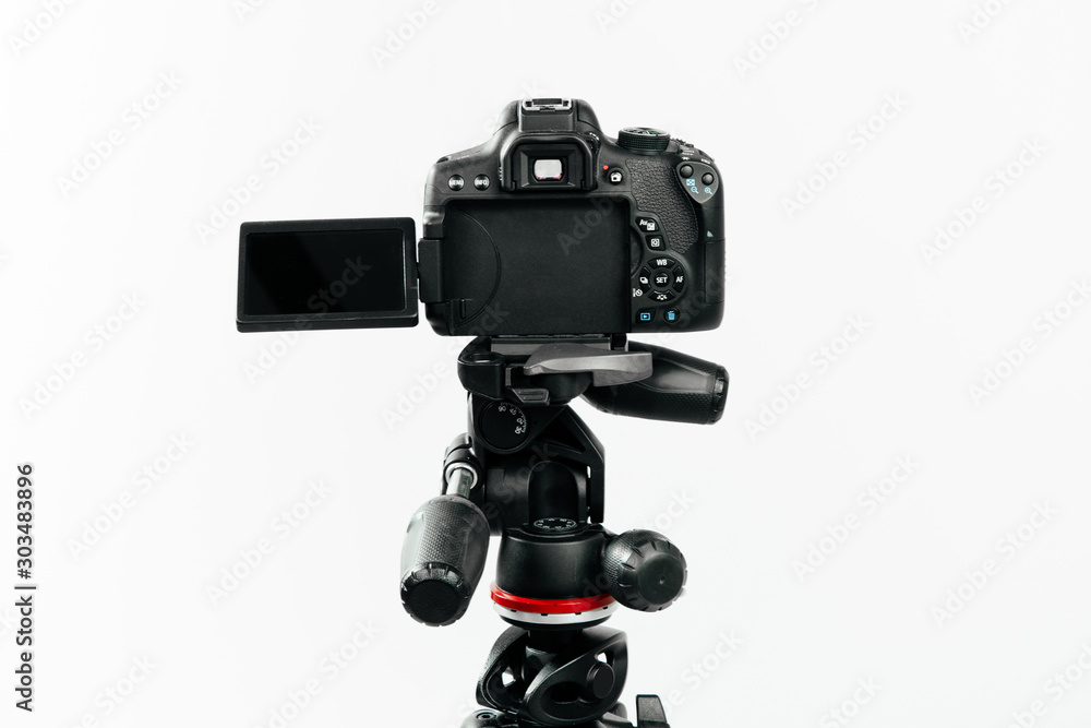 Photo camera with a tilting LCD screen on the tripod back view. Studio shot on white background