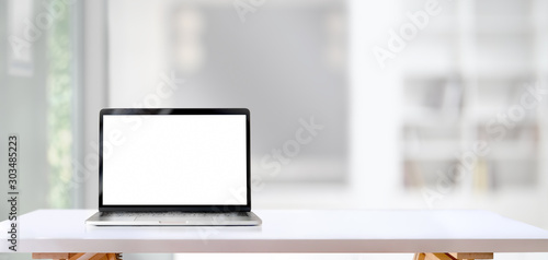 Blank screen laptop computer on white wooden table with living room in the background photo