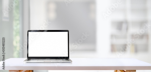 Blank screen laptop computer on white wooden table with living room in the background