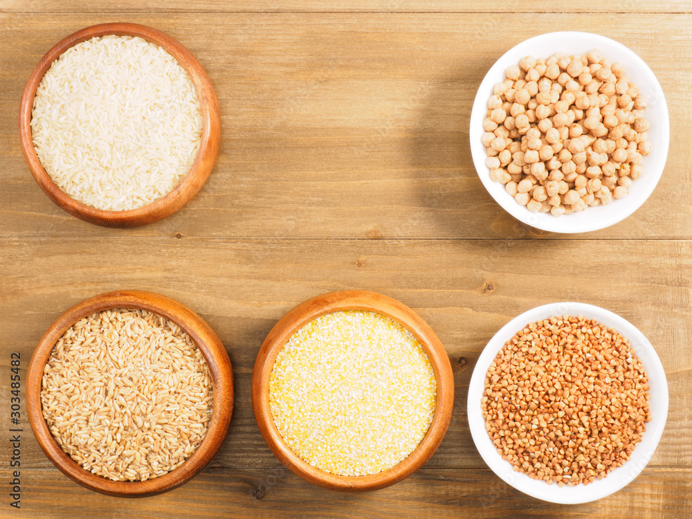 Rice, oat, buckwheat, corn flakes, chick pea in cups on brown wooden background. Indian cuisine, ayurveda, naturopathy, modern apothecary concept Rice, oat, buckwheat, corn flakes, chick pea in cups on brown wooden background. Indian cuisine, ayurveda, naturopathy, modern apothecary concept