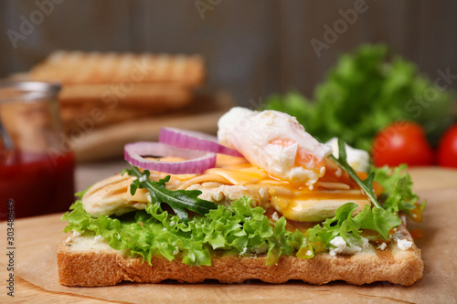 Tasty sandwich with chicken and poached egg on wooden table