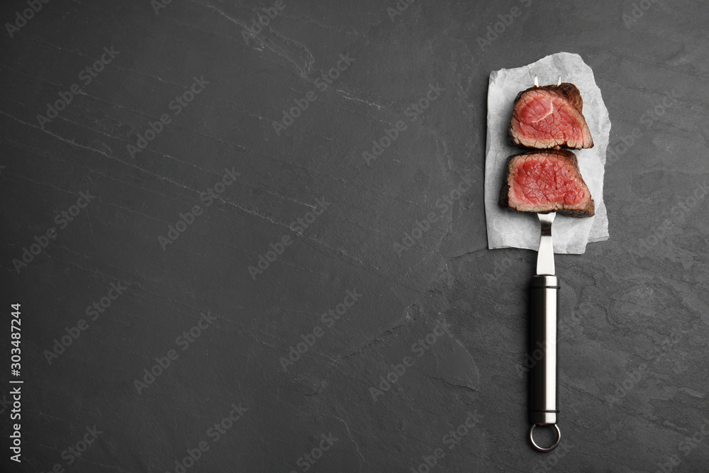 Carving fork with slices of delicious beef tenderloin on black table, top view. Space for text Carving fork with slices of delicious beef tenderloin on black table, top view. Space for text