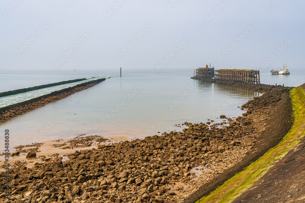 A ship passing the South Pier and a return flow into the Irish Sea, seen in Heysham Harbour, Lancashire, England, UK