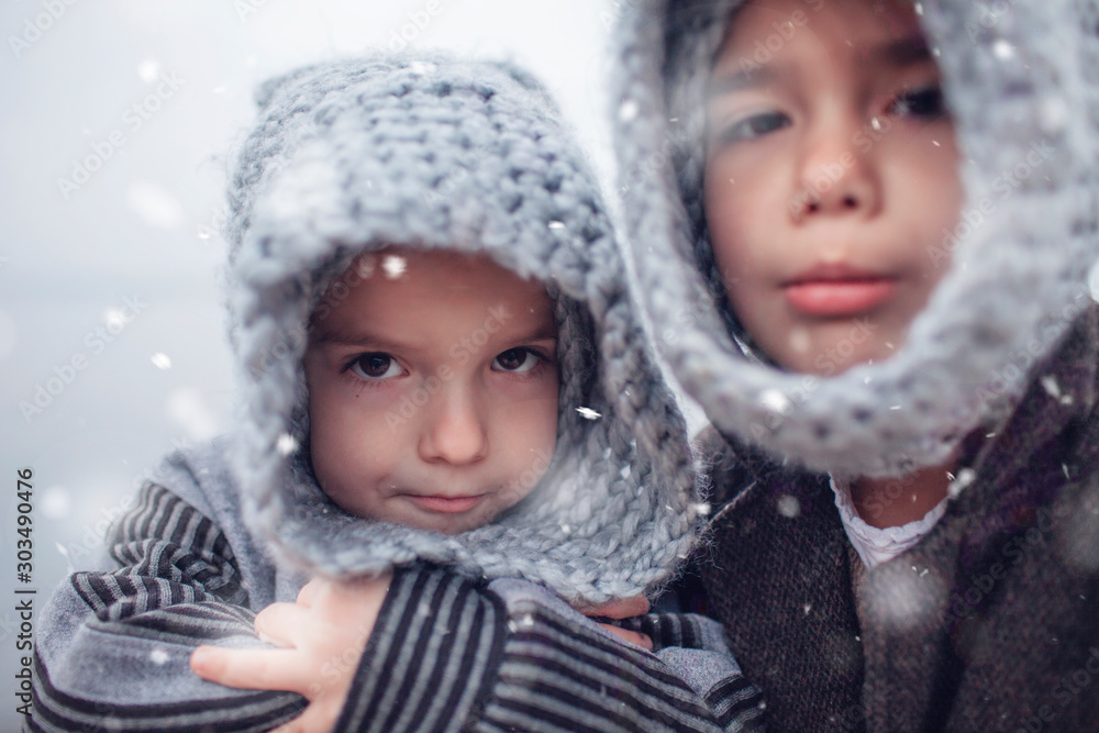 Girl in knitted grey hat hugging her frozen smaller brother Girl in knitted grey hat hugging her frozen smaller brother