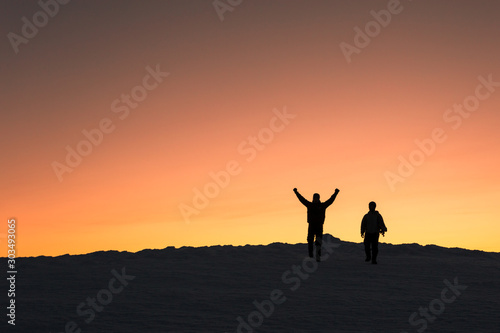 Two men descend from a winter peak at sunset