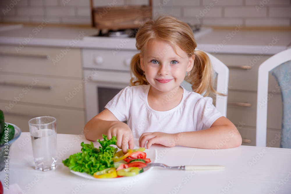 blonde baby girl eating vegetables in the kitchen