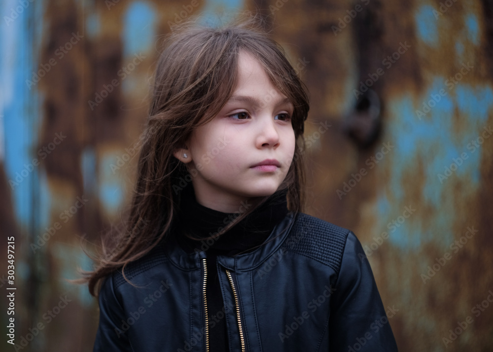 serious young girl in a black leather jacket against a rusty wall