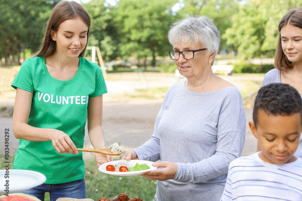 Young volunteer giving food to poor people outdoors