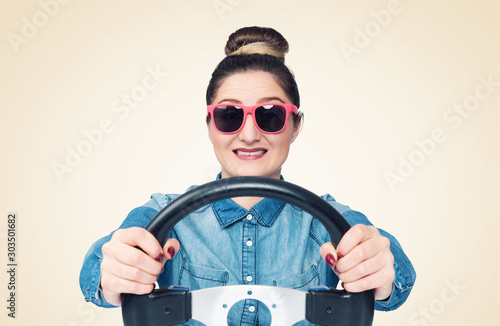 Happy young girl in sunglasses drives a car while holding a steering wheel, front view, auto concept 
