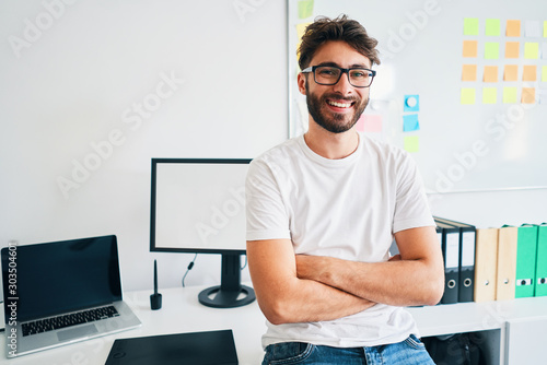 Happy young man sitting on desk in startup office