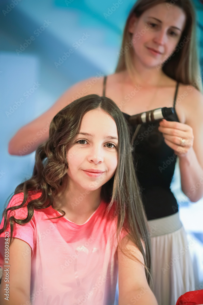 Fototapeta premium Beautiful woman curls long hair to the girl using curling iron