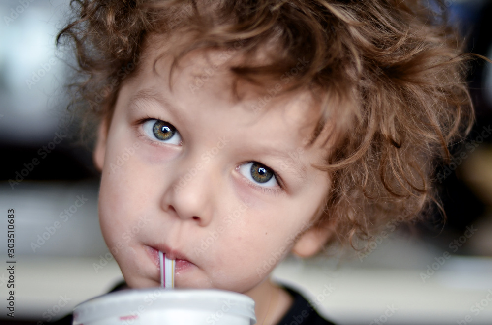 little cute boy with curly hair and big eyes drinks milk from a glass with  a straw Stock Photo | Adobe Stock