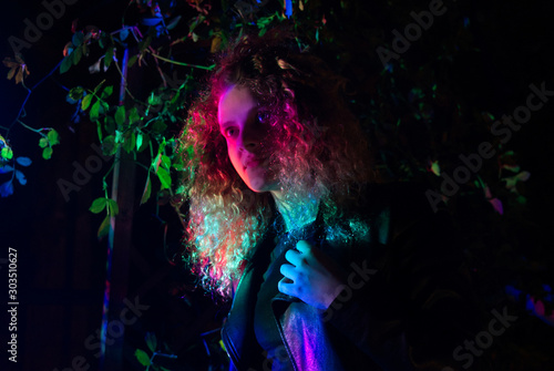 Girl in blond curly hair  illuminated by multi-colored light. 