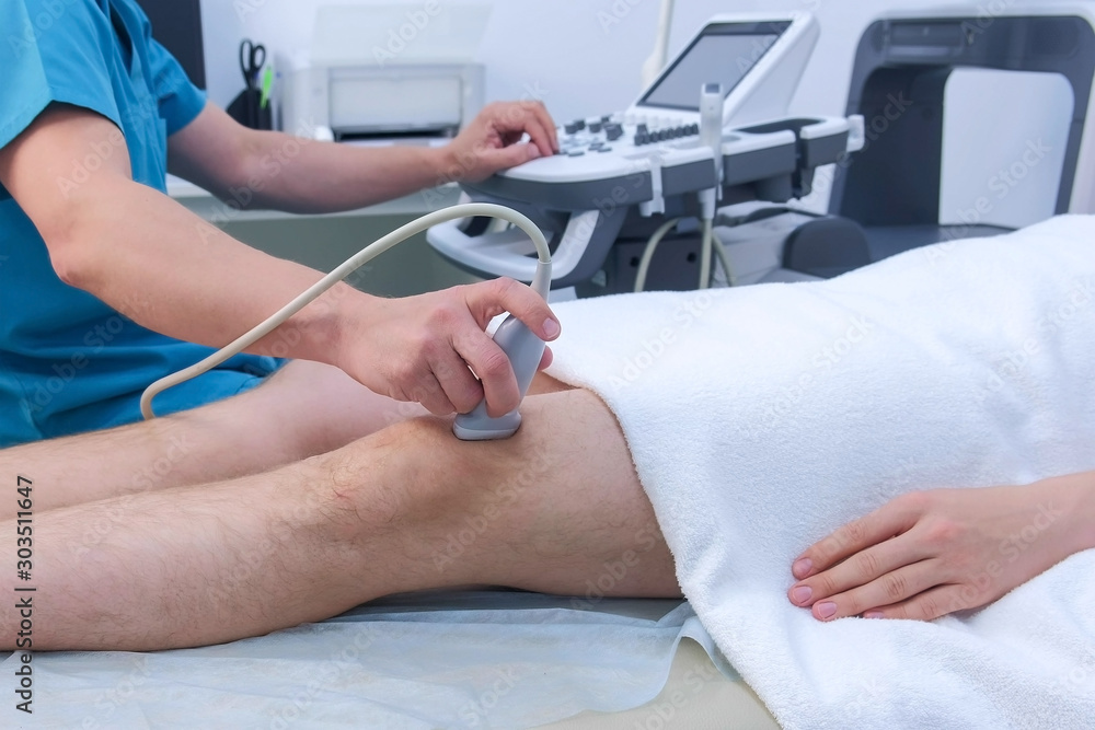 Φωτογραφία Doctor makes ultrasound of knee joint to man using ultrasound scanner in clinic, closeup leg view