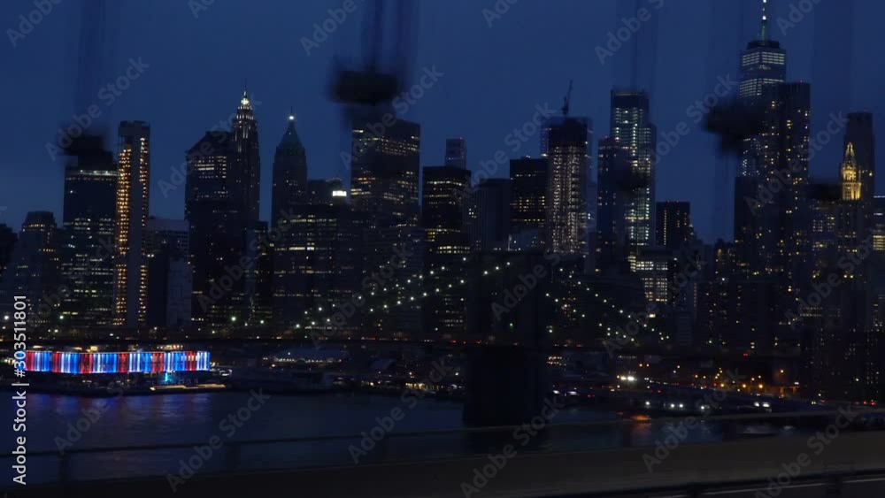 Dynamic shot of the Brooklyn Bridge at night with Manhattan skyscrapers skyline in the background, taken while crossing the Manhattan Bridge
