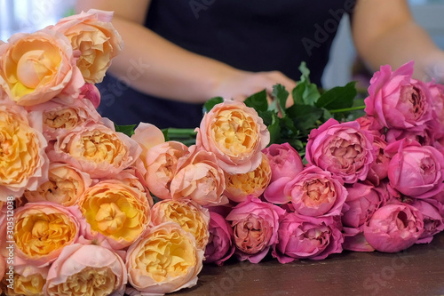 Florist woman preparing pink and orange peonies to bouquet in flower shop, hands closeup view. Floral business concept. She creates professional bunch composition in floristic studio store at table. © familylifestyle