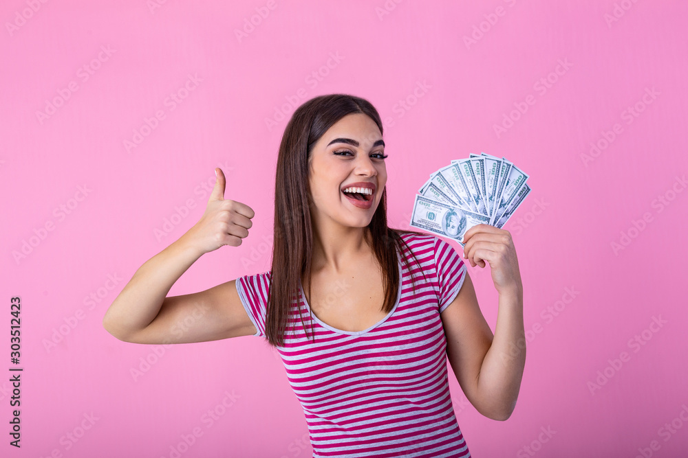 Portrait of a cheerful young woman holding money banknotes and showing thumb up isolated over pink background Portrait of a cheerful young woman holding money banknotes and showing thumb up isolated over pink background