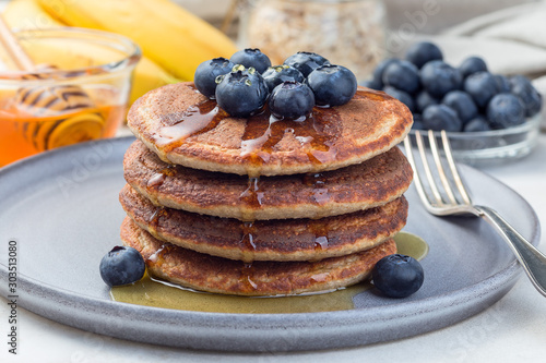 Healthy oatmeal banana pancakes garnished with blueberry and honey, on gray plate, horizontal