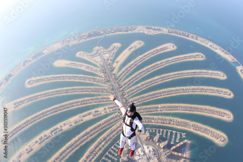 Dubai.Adrenalin flying in Skydive Dubai. Men in white suit fly above palm. 