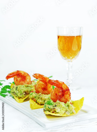 Canapes with guacamole and shrimp served on crispy tortilla chips on white serving plate