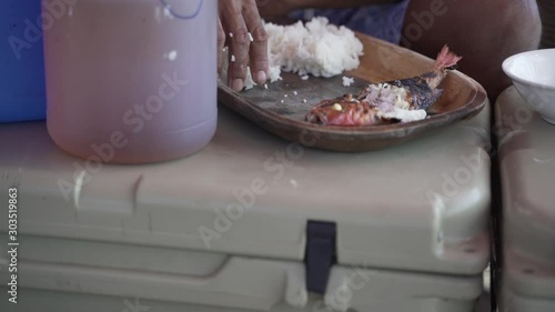 Male hand grabbing rice from wooden plate with white rice and fish photo