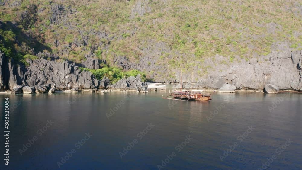 Drone flying towards tropical beach in bay with an anchored boat in front of cliffs Drone flying towards tropical beach in bay with an anchored boat in front of cliffs