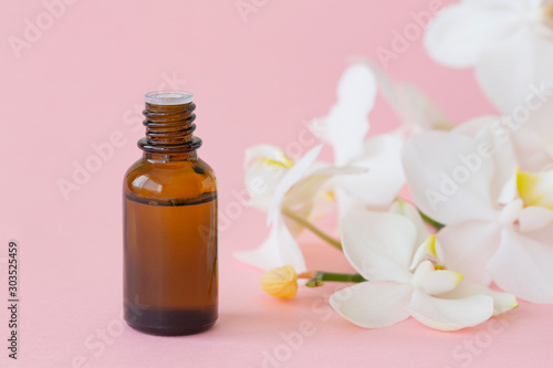 Massage oil with white orchid on pink background. Beauty concept, natural cosmetic products. Orchid extract, aromatic oils. Copy space.