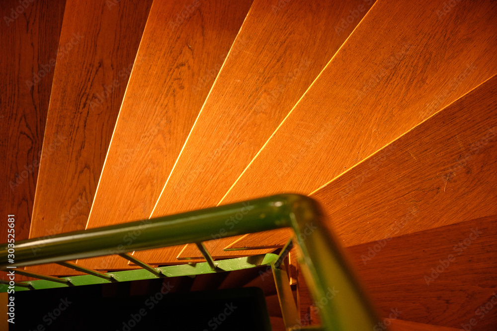 Abstract shot with a look from above on bright wooden stairs in the warm evening sunlight in a house and a green steel railing