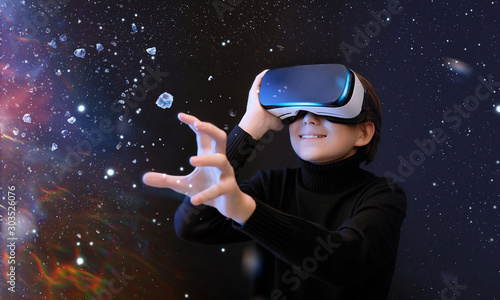 Young boy in glasses of virtual reality on dark magic universe background. Youngster using VR helmet while touching air in colorful neon lights. Augmented reality, future technology concept.