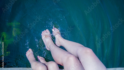 Top view of mother and her daughter have fun on pier splashing their legs into water of pond.