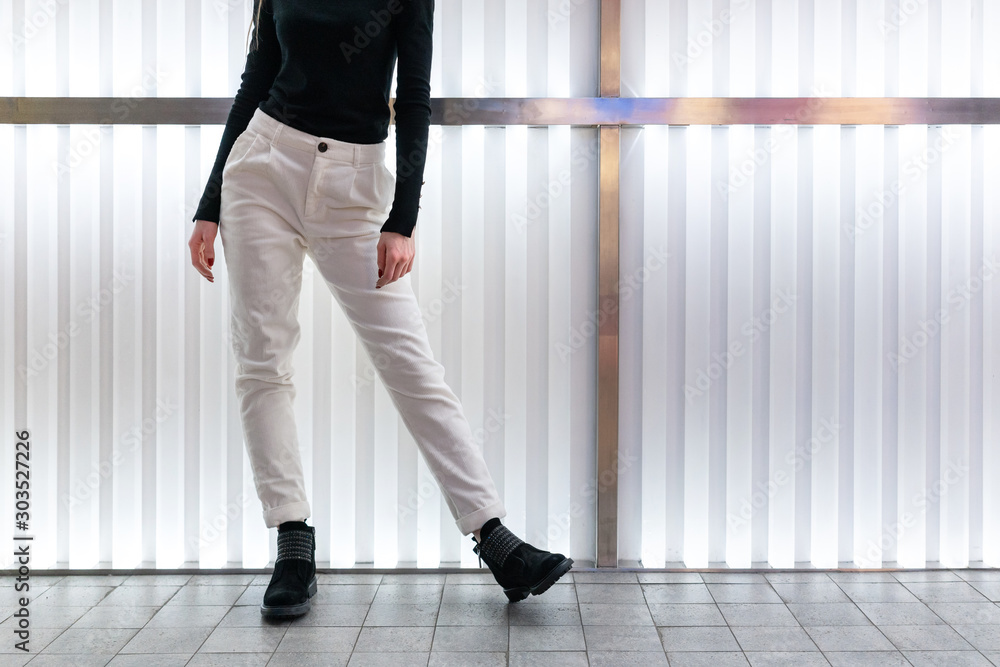 female white corduroy pants, black blouse, nubuck boots, young Caucasian model with long flowing hair posing in the interior of the light panel