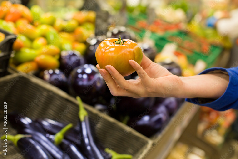 Woman's hand choosing fresh tomato in supermarket. Concept of healthy food, bio, vegetarian, diet.