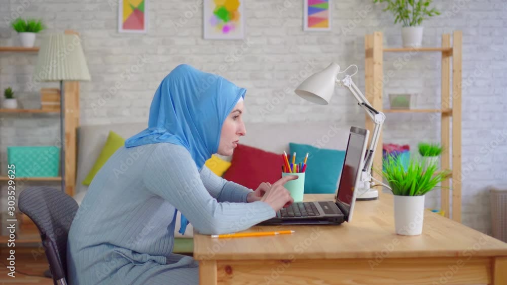young Muslim woman in a traditional headscarf slouches while sitting at a laptop and feels pain in her neck young Muslim woman in a traditional headscarf slouches while sitting at a laptop and feels pain in her neck