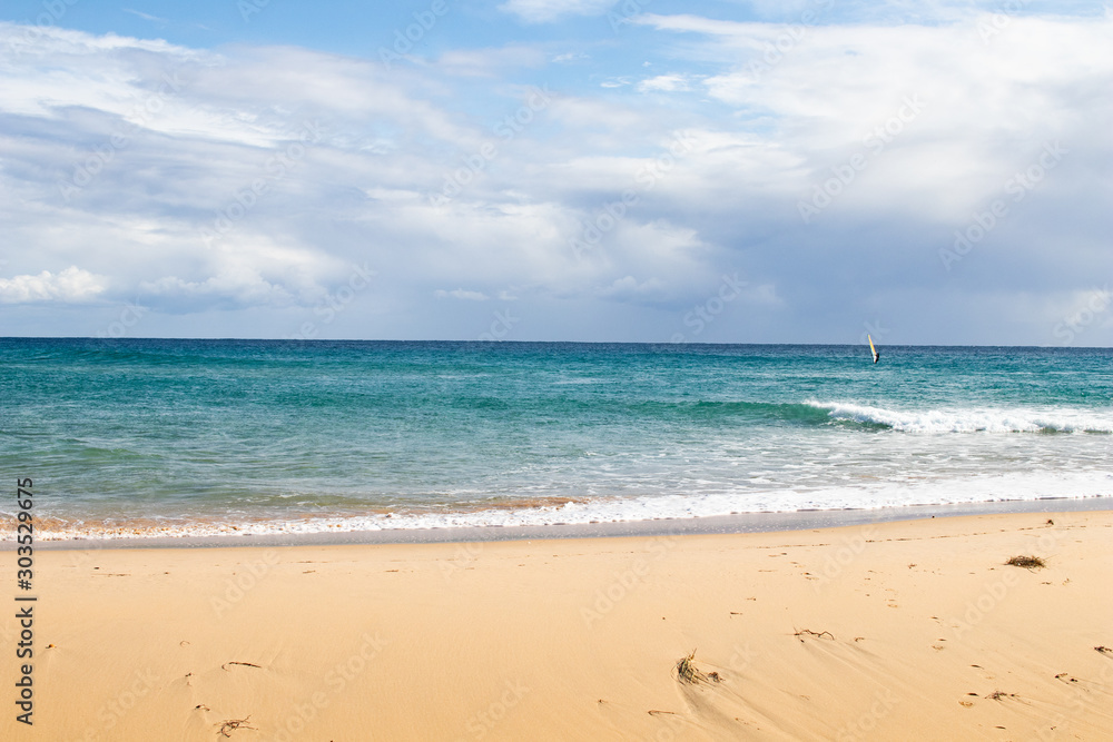 Mediterranean sea coast with beach, sun and cloudy sky. Sea and vacation in winter, yellow beach and waves that reach the shoreline. Blue and emerald green water