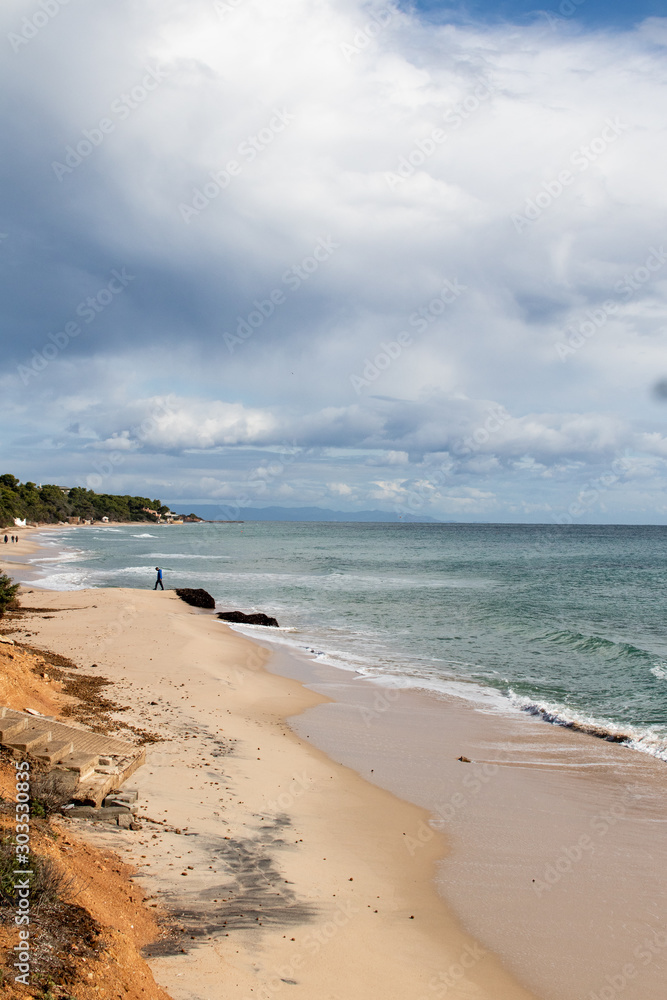 Mediterranean sea coast with beach, sun and cloudy sky. Sea and vacation in winter, yellow beach and waves that reach the shoreline. Blue and emerald green water