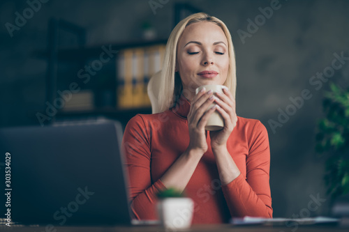 Low below angle view photo of cheerful cute nice girlfriend enjoying smell of coffee with eyes closed holding mug of tea working for transnational corporation photo