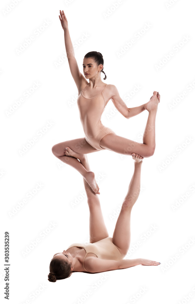 Two flexible girls gymnasts in beige leotards are performing exercises upside down using support and posing isolated on white background. Close-up. Two flexible girls gymnasts in beige leotards are performing exercises upside down using support and posing isolated on white background. Close-up.