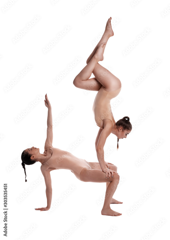 Two flexible girls gymnasts in beige leotards are performing exercises upside down using support and posing isolated on white background. Close-up.