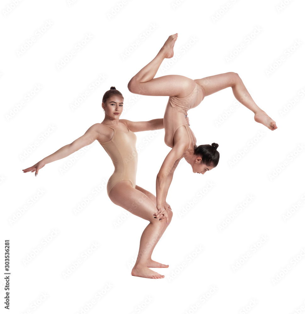 Two flexible girls gymnasts in beige leotards are performing exercises using support and posing isolated on white background. Close-up. Two flexible girls gymnasts in beige leotards are performing exercises using support and posing isolated on white background. Close-up.