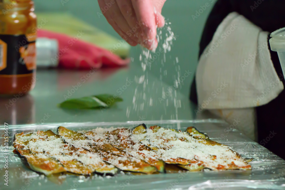 Male hand preparing a dish of aubergines with grated cheese
