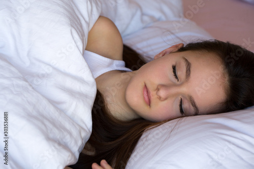 Sleeping teen girl enjoying healthy nap in cozy bed in the morning, millennial girl relaxing on soft pillow and comfortable mattress with white cotton.