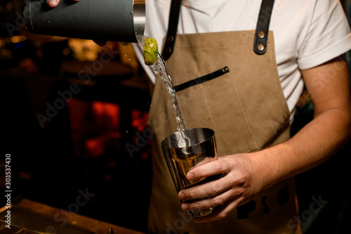 Professional bartender pouring a cocktail with lime and alcoholic drink from the one part of steel shaker to another