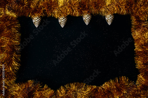 Beautiful christmas concept. Gold tinsel with cones on black background as frame. Copy Space. Christmas flat lay. photo