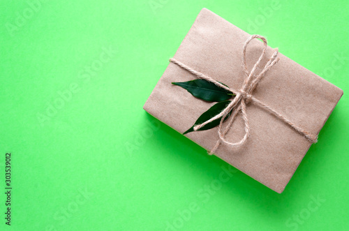 Gift box wrapped in kraft paper tied with twine and decorated with two green leaves on a light green background. Zero waste holidays concept. DIY present idea. Copy space. Flat lay