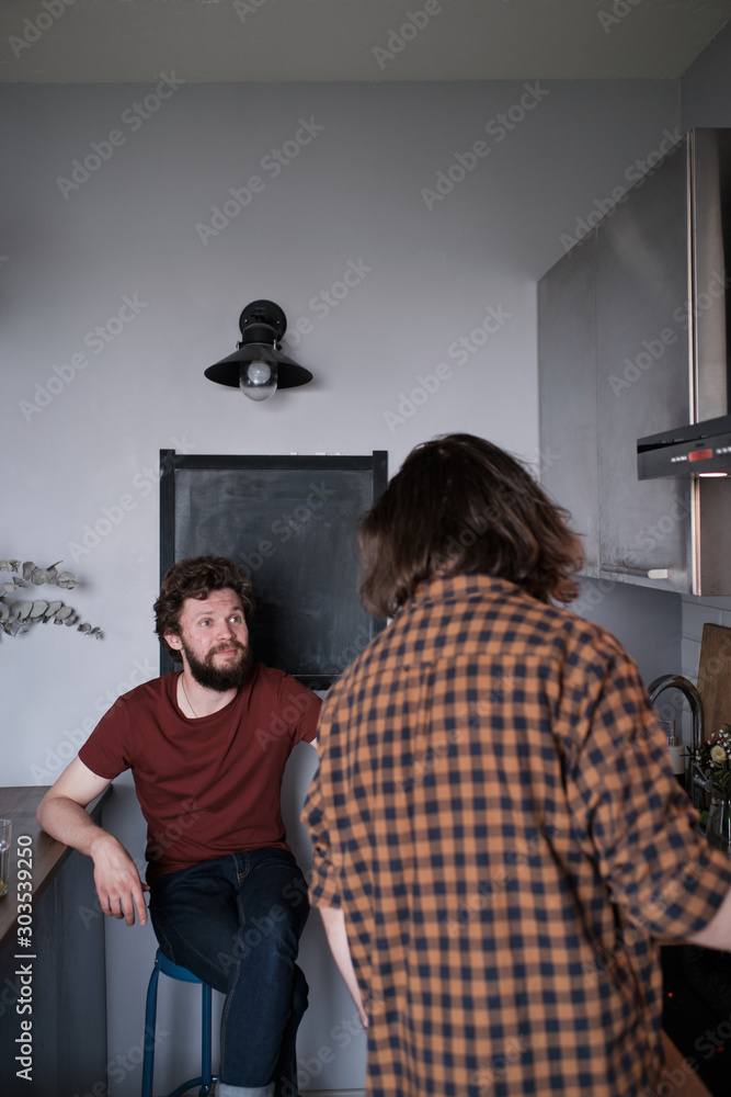 Two men talking in the kitchen while one is cooking Two men talking in the kitchen while one is cooking