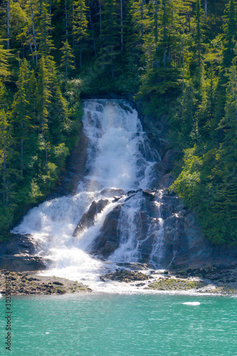 Waterfall sending torrents of water from mountains above, into oceans of Alaska.