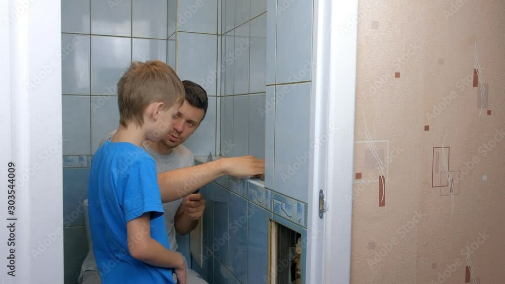 Dad and son make repairs together at home, remove tiles from walls in toilet. Father man explaining boy how to use tools. Self made home repair. Family engaged in construction and renovation work. Dad and son make repairs together at home, remove tiles from walls in toilet. Father man explaining boy how to use tools. Self made home repair. Family engaged in construction and renovation work.