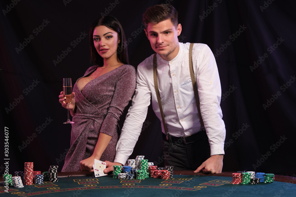 Guy in white shirt is playing poker at casino, at table with stacks of chips on it. He celebrating win with sexy female. Black background. Close-up. Guy in white shirt is playing poker at casino, at table with stacks of chips on it. He celebrating win with sexy female. Black background. Close-up.