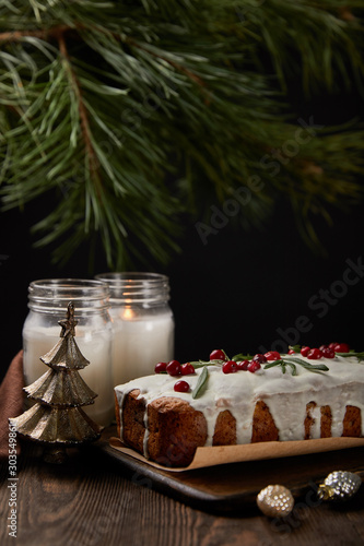 traditional Christmas cake with cranberry near pine, baubles and candles on wooden table